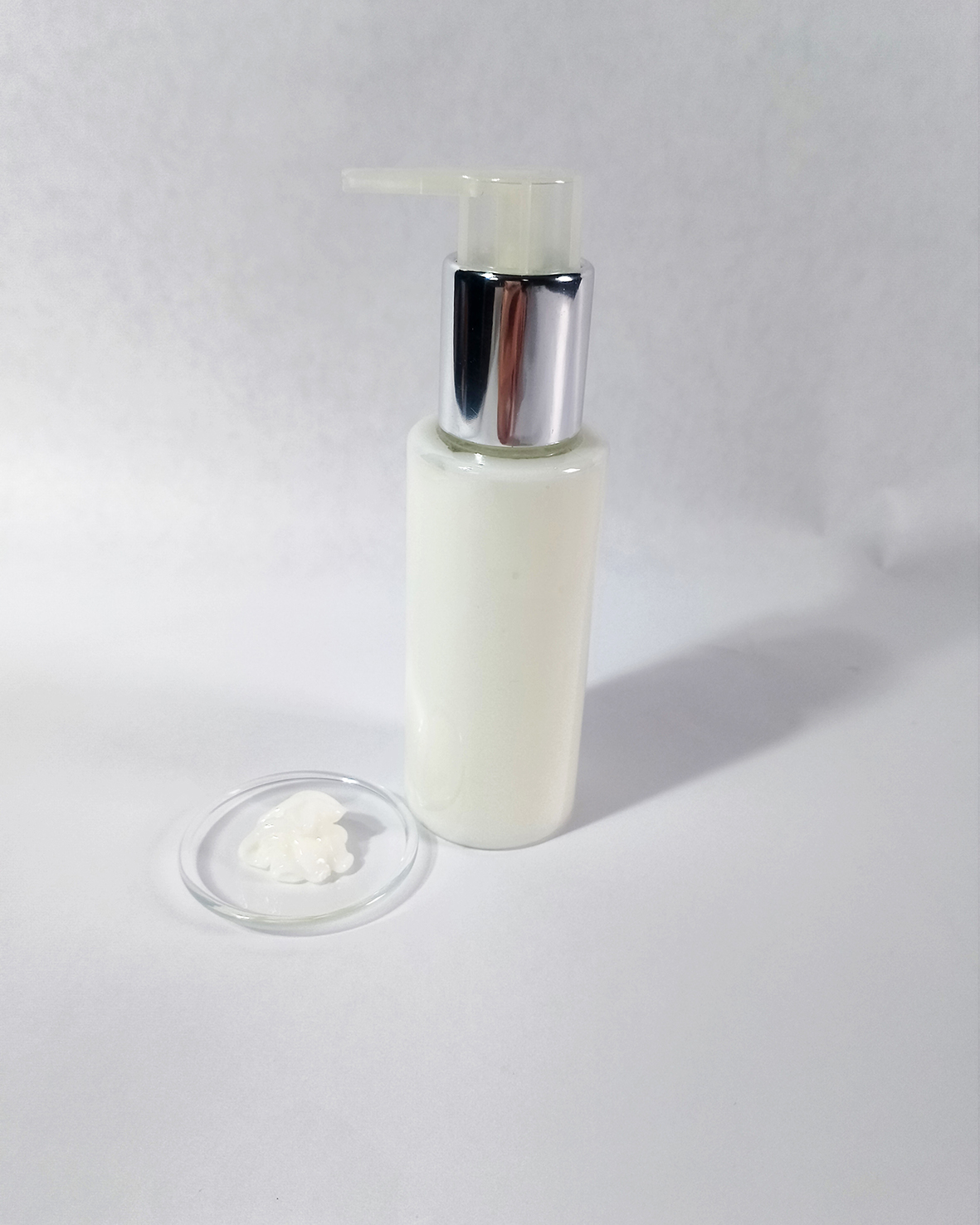 Sklenená fľaška s chmeľovým kondicionérom a tekutinou na priehľadom akrylovom podnose na bielom pozadí.